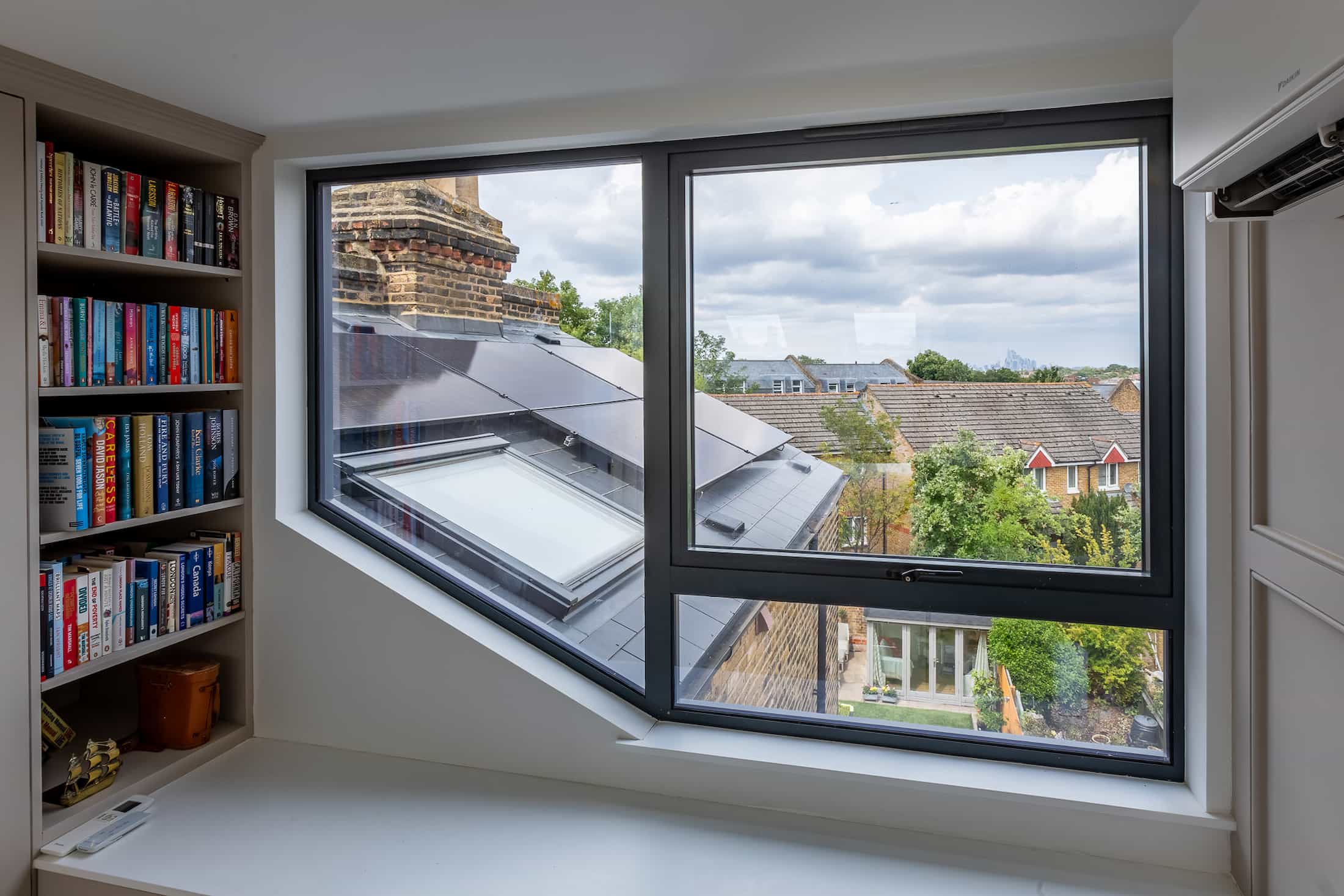 Bright loft hallway with a large skylight window in a sloped ceiling, white walls, and framed artwork.