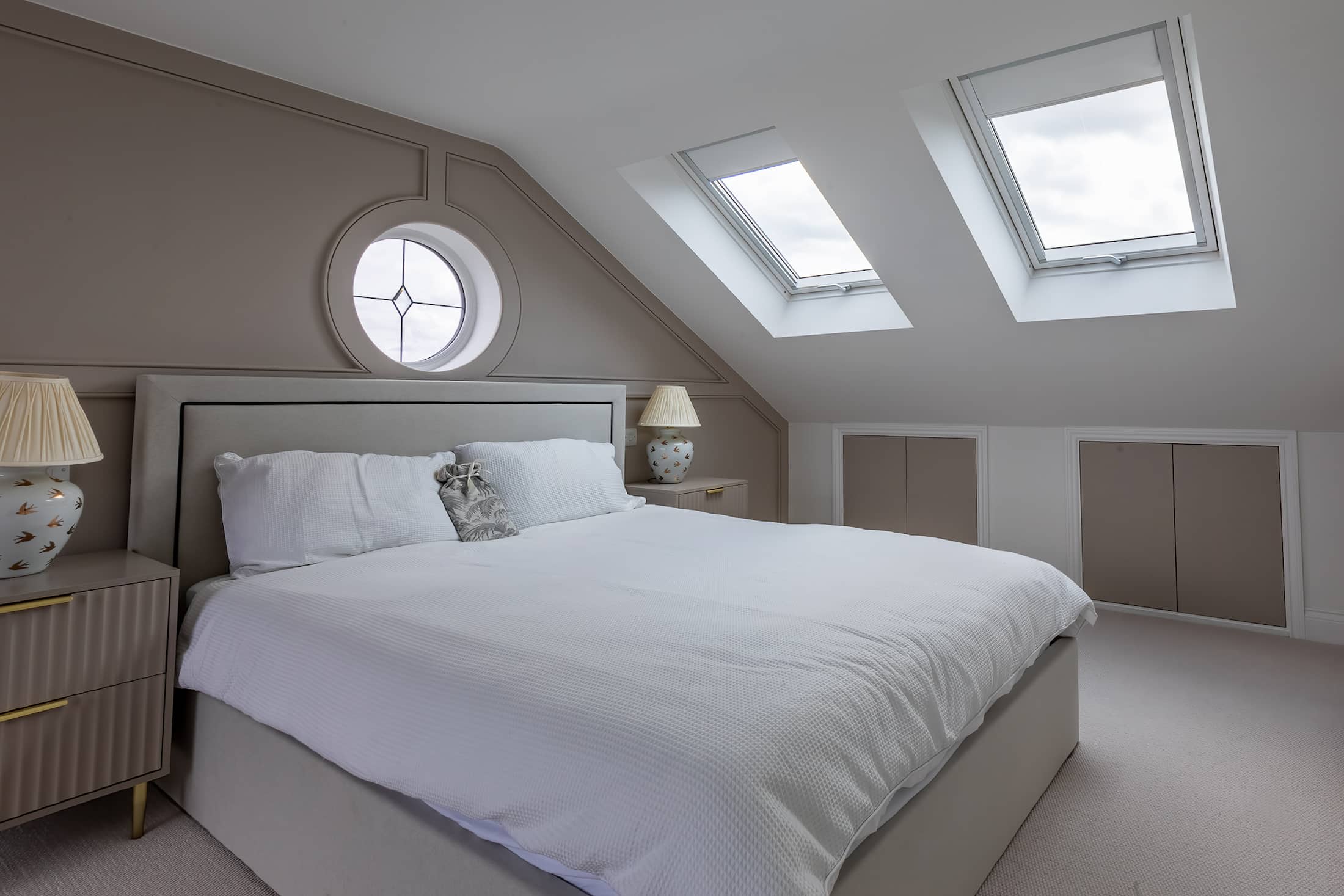 Spacious loft bedroom with a large bed, neutral decor, sloped ceiling, circular feature window, and skylights.
