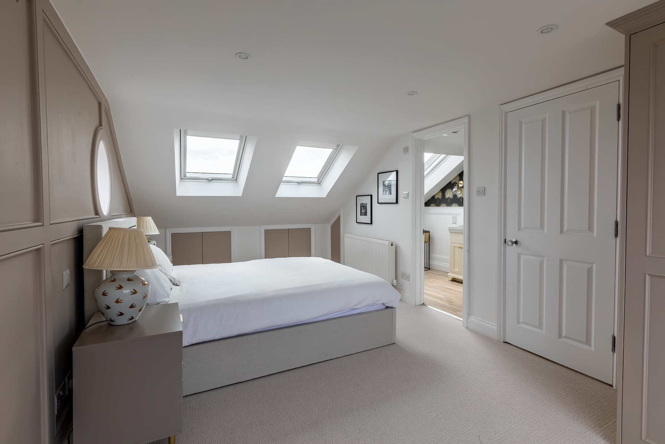 Bright loft bedroom with two skylight windows, built-in storage, neutral tones, and doorway leading to an ensuite bathroom.